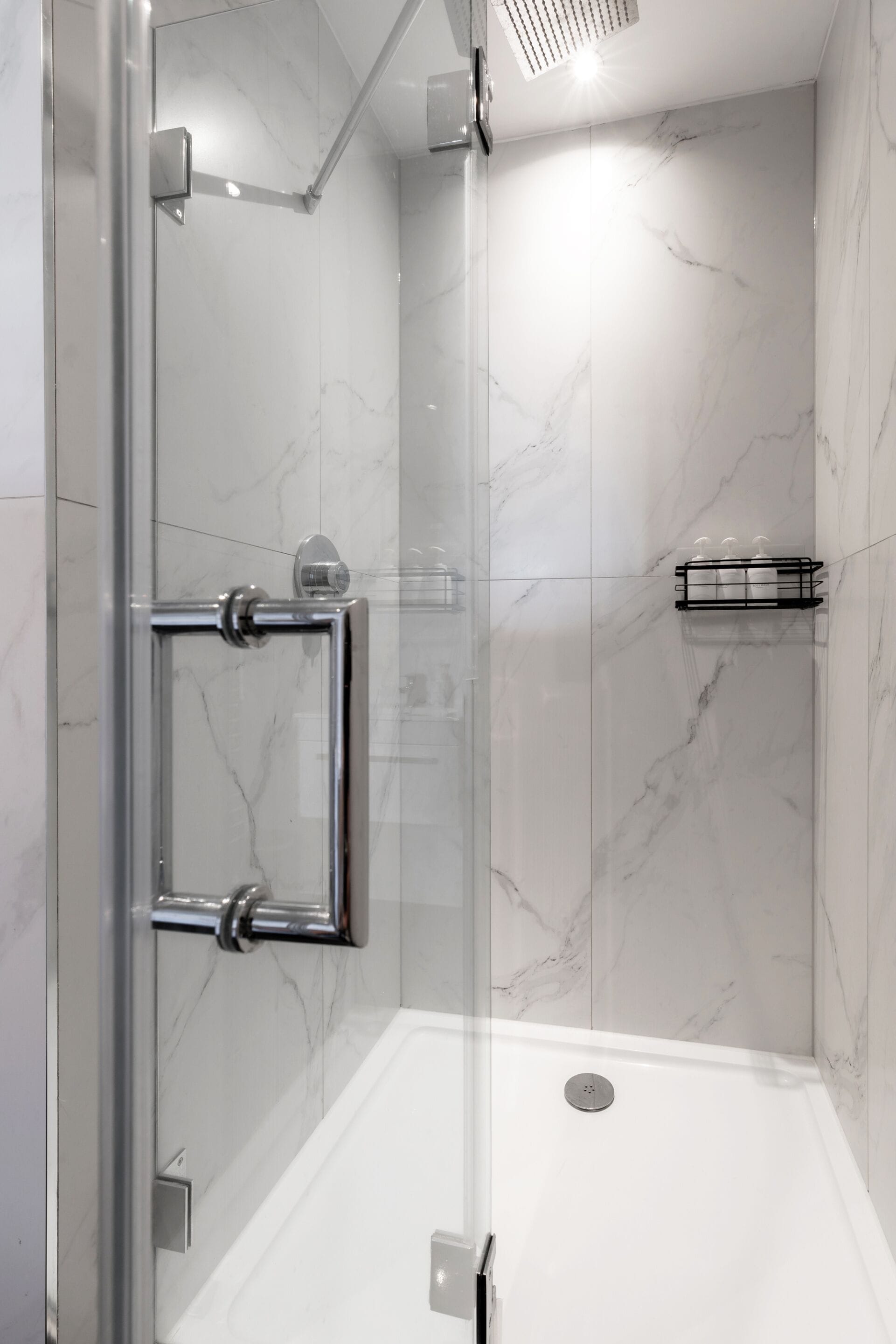 A glass-enclosed shower with a marble wall, a glass door, and a metal towel rack.
