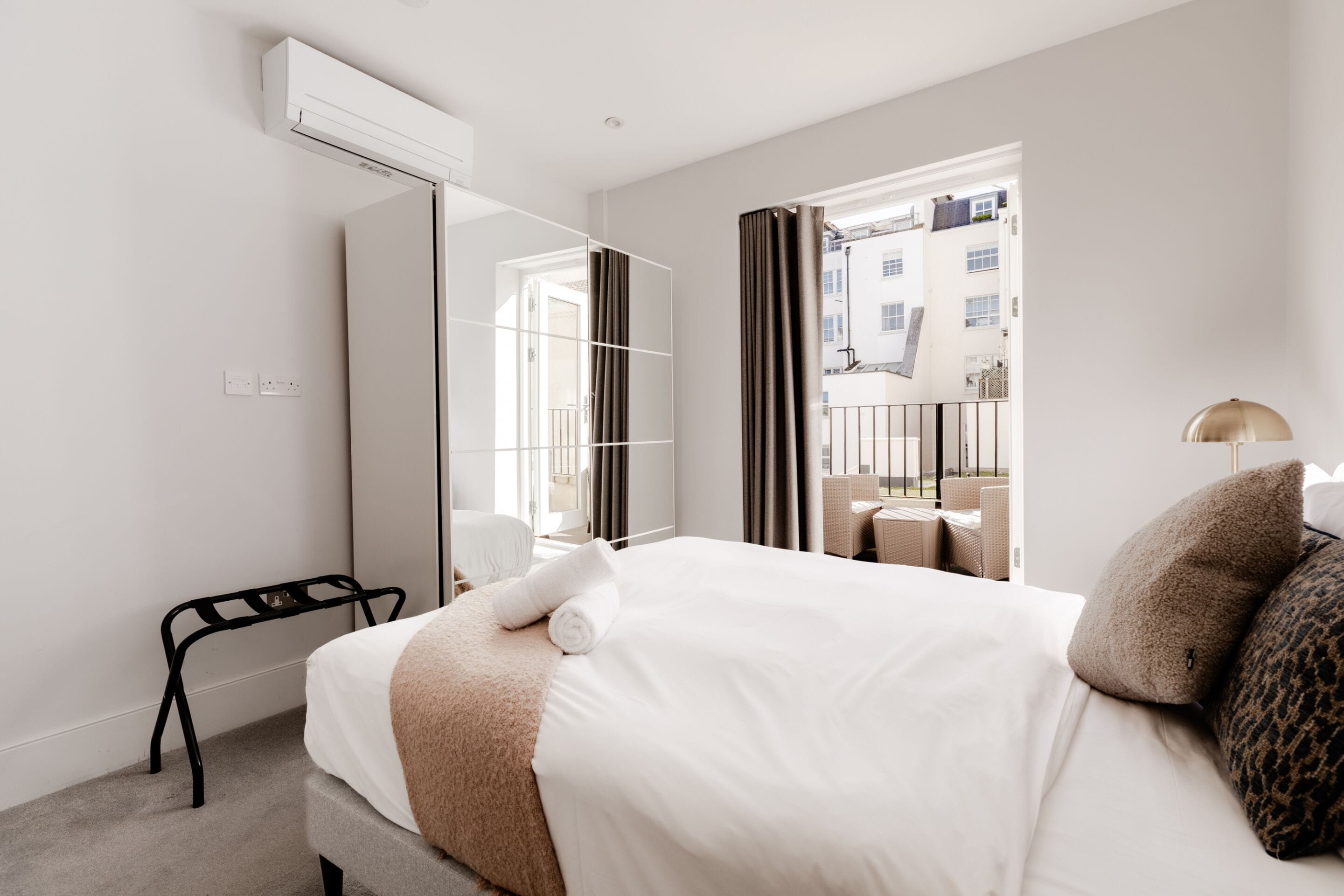 A hotel room with a large bed, a mirror, a small table, and a balcony with a view of buildings.