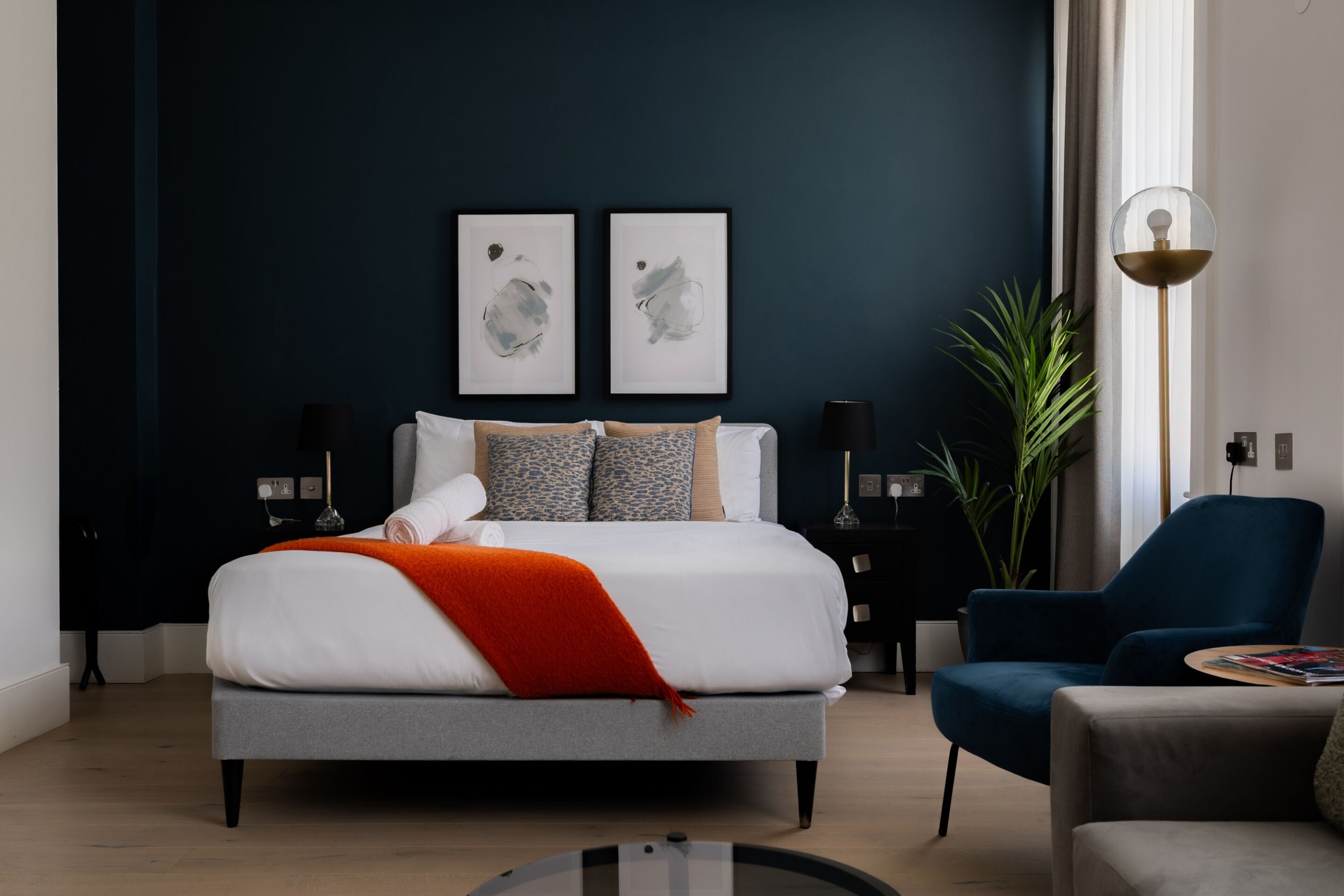 A modern bedroom with a bed, bedside tables, a blue armchair, and a floor lamp.