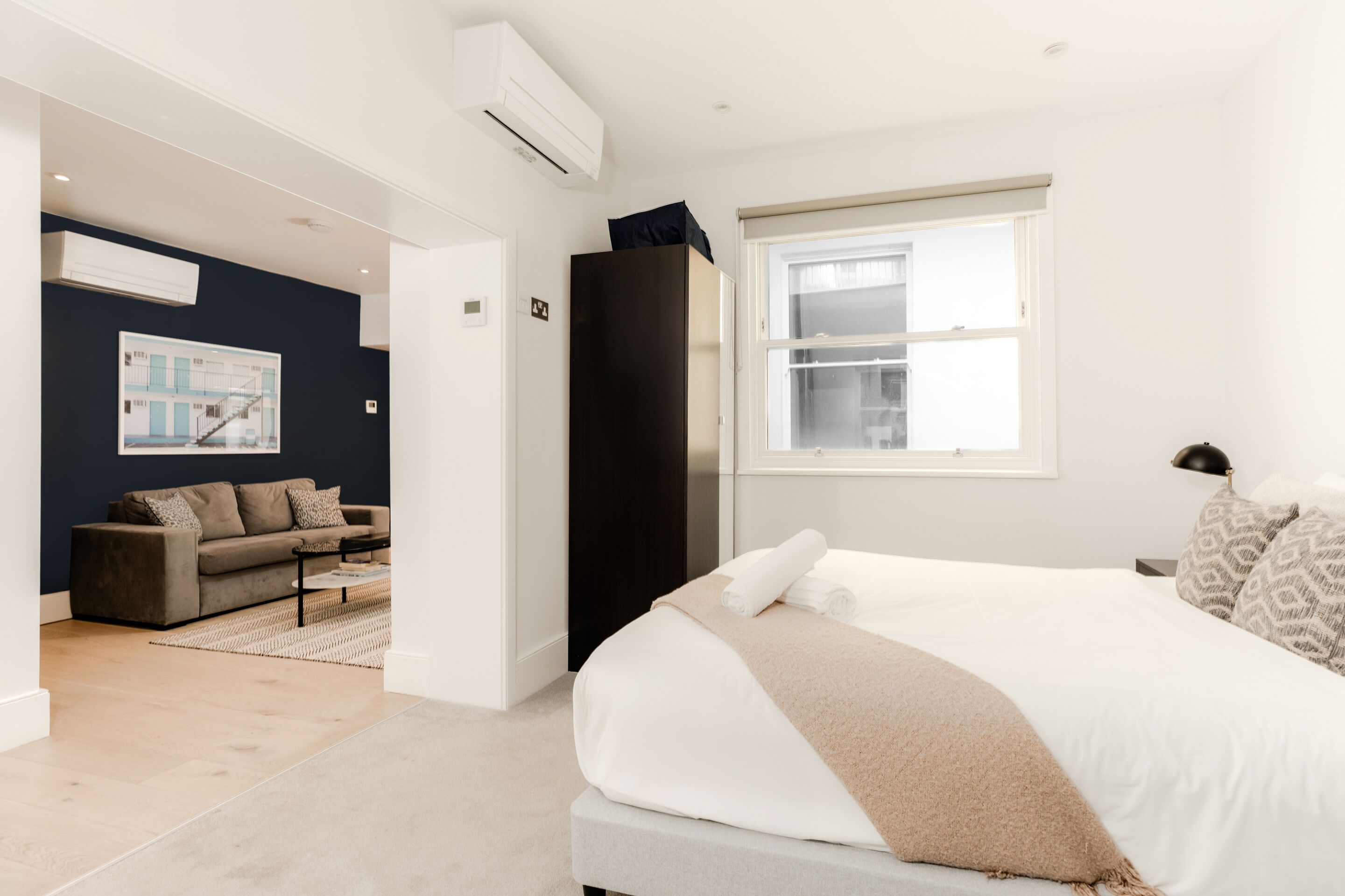 Une chambre d’hôtel moderne avec un grand lit, une armoire de couleur sombre, un ensemble de canapés et une grande fenêtre.