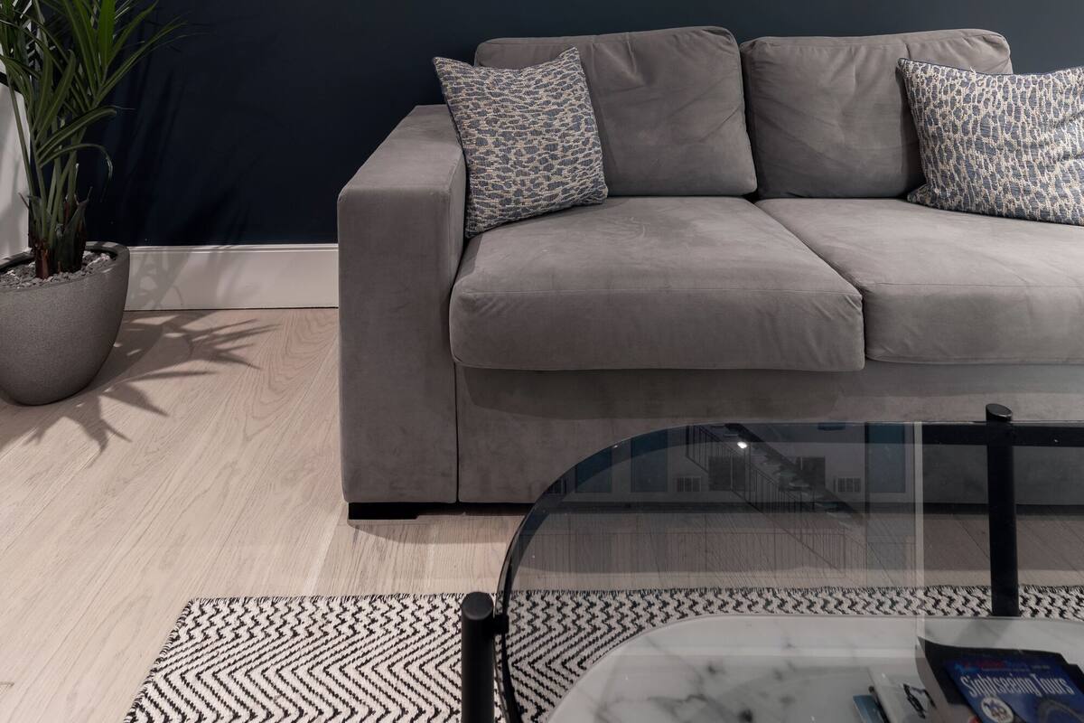 A modern living room with a grey sofa, patterned cushions, a potted plant, and a framed cityscape artwork on the wall.