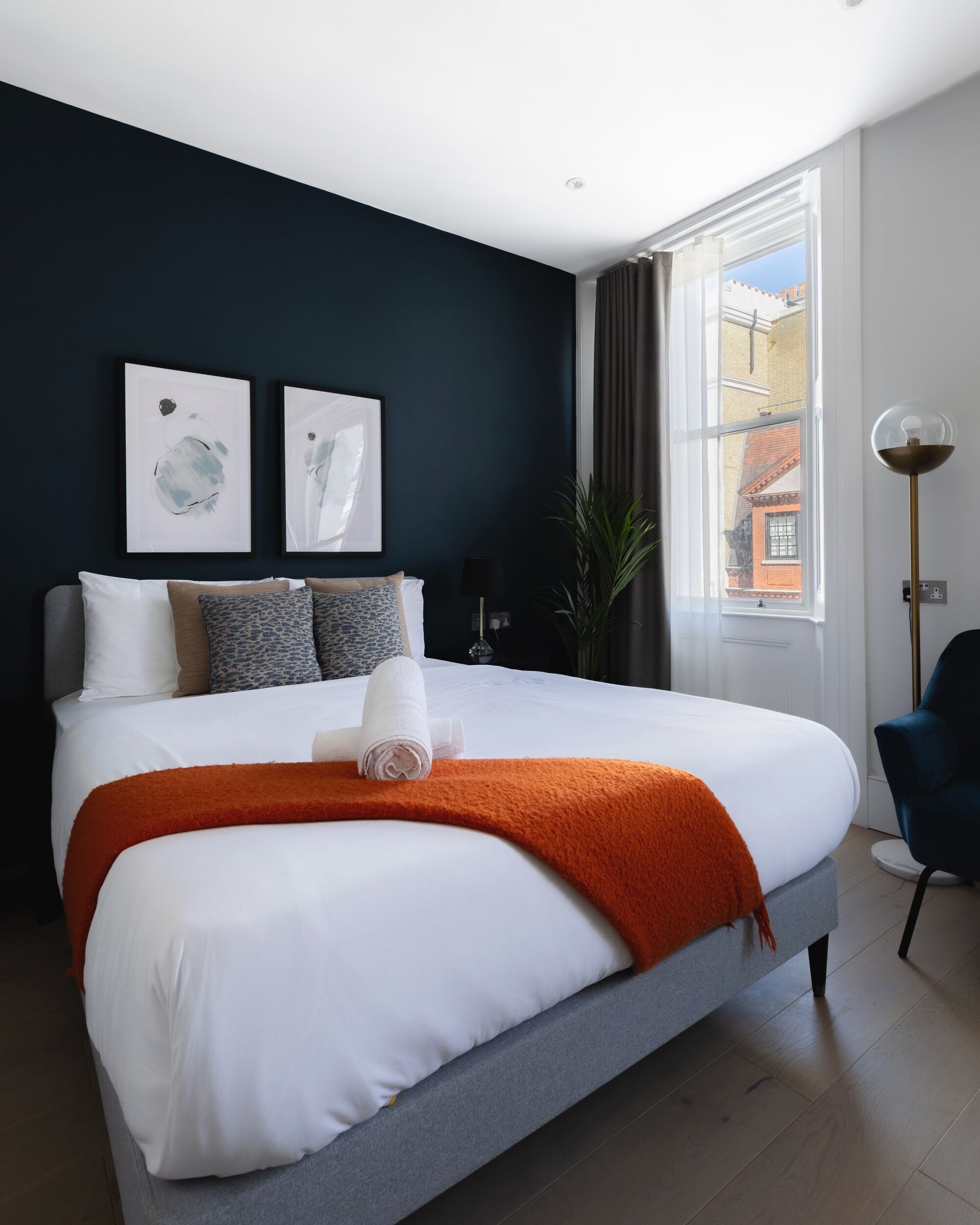 A modern hotel room with a large bed, dark walls, and a view of the city through a window.