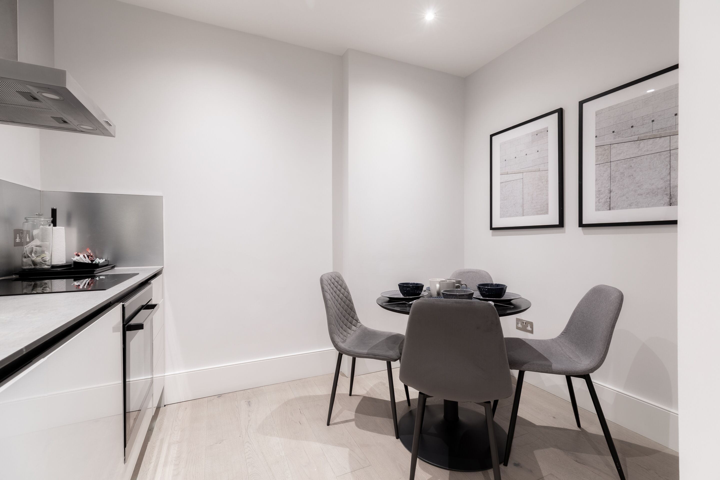 A modern kitchen with a dining area, featuring a black countertop, grey chairs, and two framed pictures on the wall.