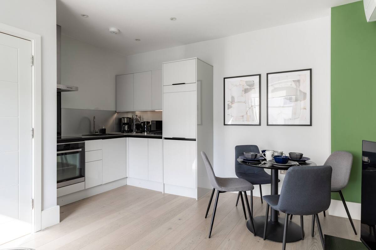 A modern kitchen with white cabinetry, a black countertop, and a dining area with a table and chairs.