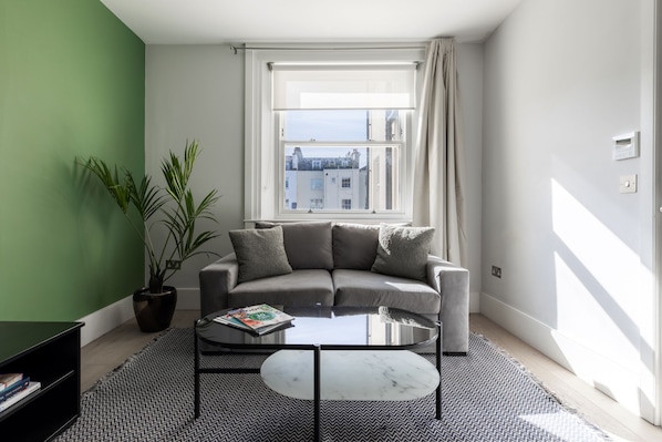 Una sala de estar moderna con un sofá gris, una mesa de centro de vidrio y una planta en maceta.