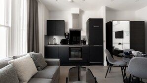 Une cuisine moderne avec des meubles de couleur sombre, un four encastré et une machine à café. On y trouve également un coin repas avec une table et des chaises.