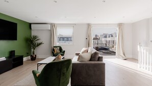 Un salon moderne avec un fauteuil vert, un canapé gris et un téléviseur à écran plat fixé sur un mur vert.