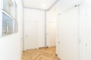 A hallway with white doors, a wooden herringbone floor, and a geometric pendant light.