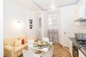 A compact living space with a dining table, sofa, kitchenette, and a door leading to a balcony.