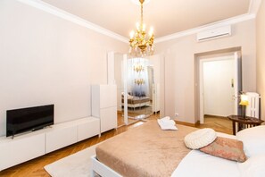 A bedroom with a bed, a TV, a chandelier, a mirror, and a door.