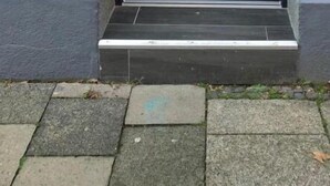 A black door with a geometric design, a metal handle, and a small step leading to the entrance. - Apartment COLIN (Bremerhaven)