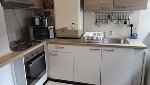 A compact kitchen with a microwave, toaster, stove, oven, and a sink with hanging utensils. - Apartment COLIN (Bremerhaven)