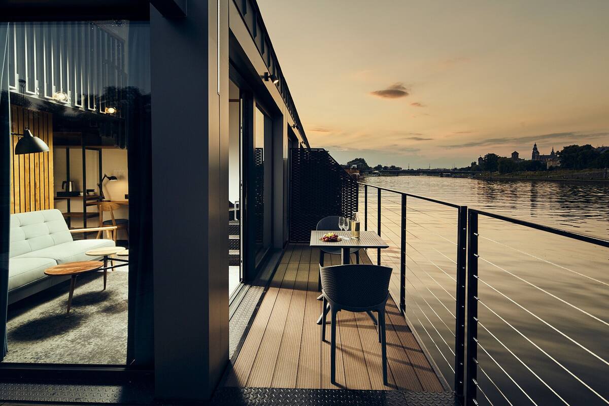 A modern balcony with a view of a river and a cityscape at sunset.