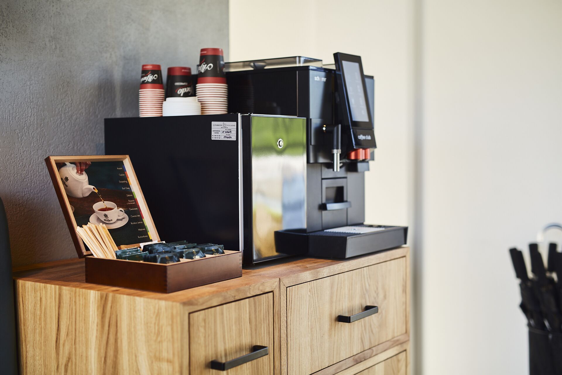 A coffee machine on a wooden counter with a framed picture of a tea set.