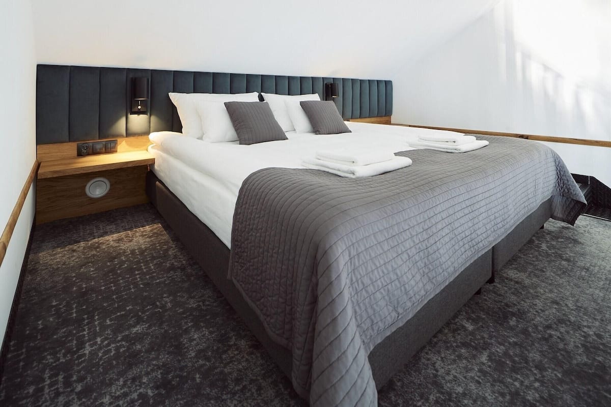 Een hotelkamer met een bed, nachtkastje, lamp en een wandlamp.