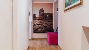 A hallway with a large photo of the Colosseum, a red ottoman, and a framed picture on the wall.