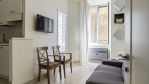 A modern living room with a sofa, two wooden chairs, a flat-screen TV, and a window with curtains.
