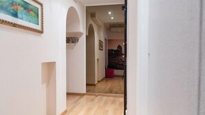 A hallway with wooden flooring, white walls, and a framed painting. There is a door on the right and a staircase leading to another room.