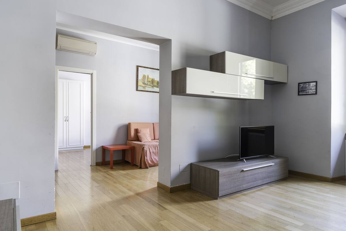 A modern living room with a flat-screen TV, built-in cabinets, and a wooden floor.