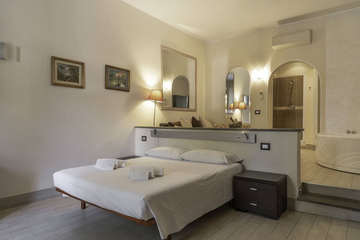 A hotel room with a bed, bedside tables, a mirror, a shower, and a toilet.