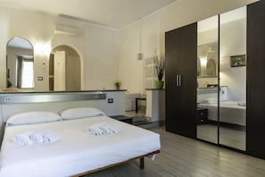 Une chambre d’hôtel avec un grand lit, une armoire, un miroir et une petite table sur laquelle est posée une plante.