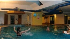 Ein Hallenbad mit einer schwimmenden Person und einer weiteren Person im Wasser.