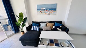 Un salon moderne avec un canapé, une table basse et un tableau représentant une scène de plage.
