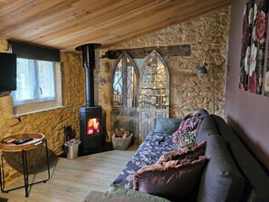 Una sala de estar acogedora con pared de piedra, techo de madera, chimenea, un sofá con cojines y una mesita con un control remoto.
