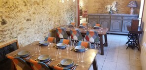 A dining area with a rustic stone wall, wooden tables set for a meal, and a vintage sewing machine in the corner. - Storybook French Watermill plus Gîte with Private Pool close to tourist sites (Pays de Belves)