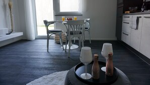 A modern kitchen with a dining area, featuring a table with chairs, a window with curtains, and a tray with glasses and a bottle. - Ferienhaus mit 6 Apartments, Terrasse und Blick auf den Stausee (Bad Lobenstein)