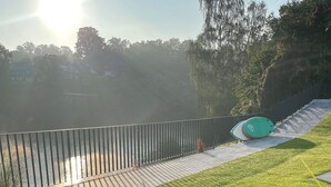 A well-maintained grassy area with a metal fence, a pathway, and a green object on the ground. - Ferienhaus mit 6 Apartments, Terrasse und Blick auf den Stausee (Bad Lobenstein)