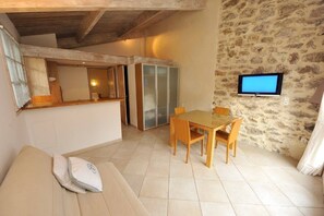 A cozy room with a sofa, a dining table with chairs, a television mounted on the wall, and a stone wall.