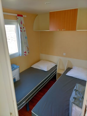 A small, compact room with two bunk beds, a window with a curtain, and a small table with a bag.