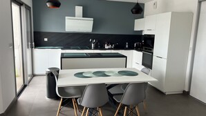 Una cocina moderna con una mesa blanca, sillas grises y una encimera negra.