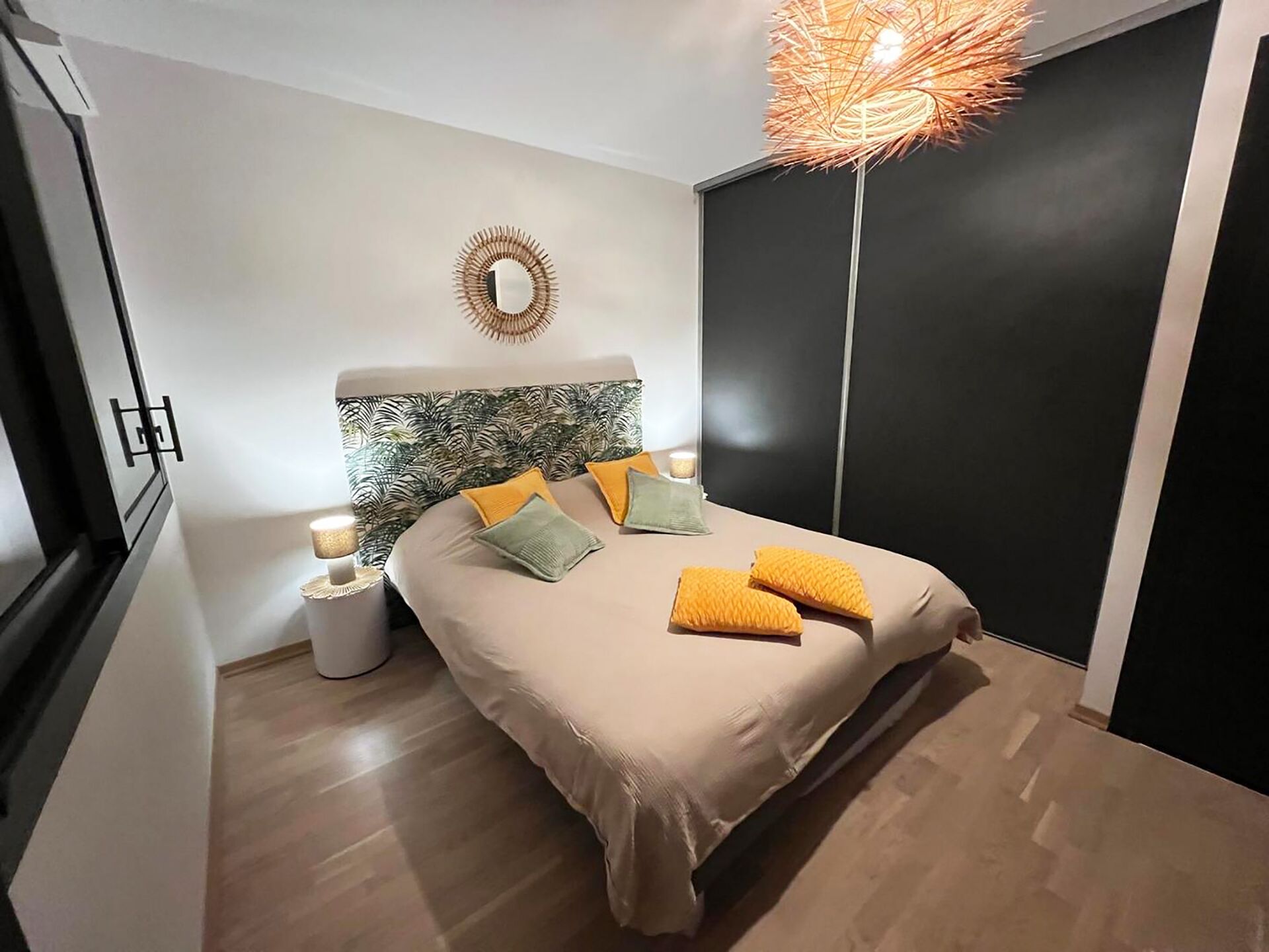 A modern bedroom with a bed, bedside lamps, a decorative mirror, and a unique ceiling light fixture.