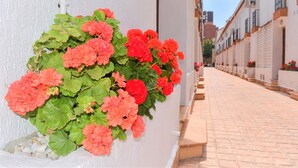 A narrow street with a row of white buildings, a paved walkway, and a planter with red flowers. - Ola Azul bungalow V (Benidorm)