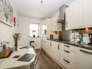 Een moderne keuken met witte kasten, een magnetron, een Bosch koffiezetapparaat en een raam met een bloevas.