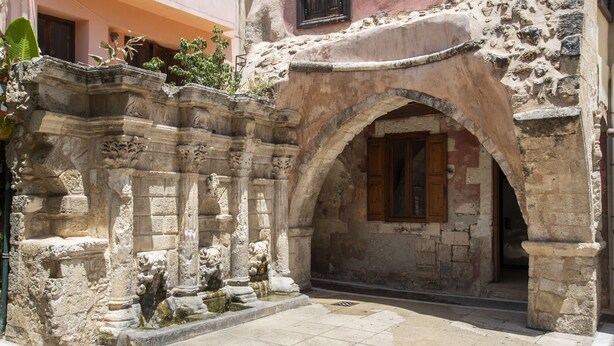 Un arc en pierre d’époque, menant à l’entrée d’un bâtiment, est encadré par un mur de pierre orné de sculptures décoratives.