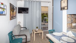 Un espace de vie compact comprenant un canapé, une table à manger et des chaises. Un téléviseur est fixé au mur, et une petite table avec une télécommande est également présente.