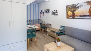 Un espace de vie compact comprenant un coin repas, un canapé et un tableau représentant un coucher de soleil.