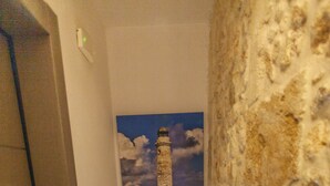 Un escalier, avec un mur de pierre d’un côté et une porte de l’autre, mène à une pièce où est accrochée une photographie encadrée représentant un phare.