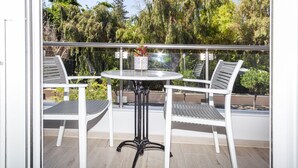 Un balcon avec une table ronde et deux chaises, une balustrade en verre et une vue sur les arbres.