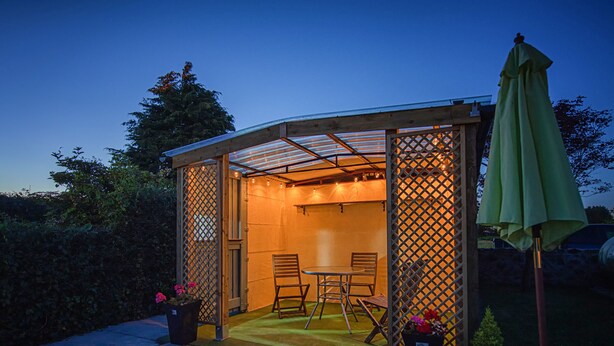 Un espace extérieur abrité, aménagé avec une table et des chaises, et entouré d’une clôture en bois agrémentée de panneaux en treillis.