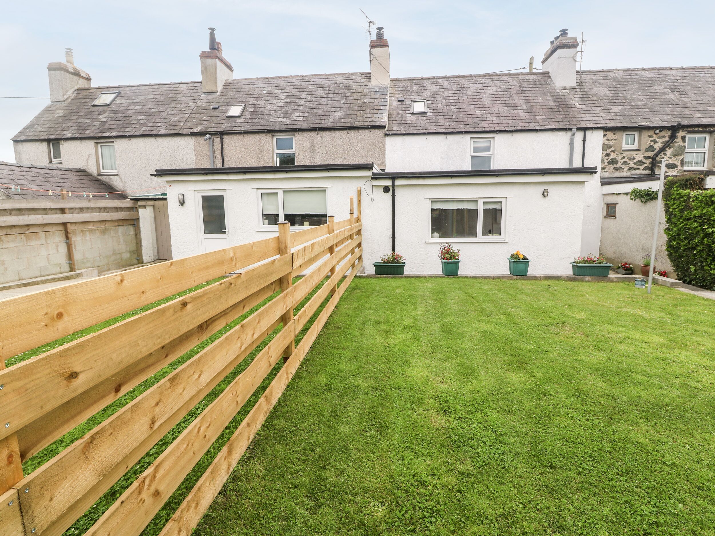 A residential property with a well-maintained lawn, a wooden fence, and a row of potted plants.