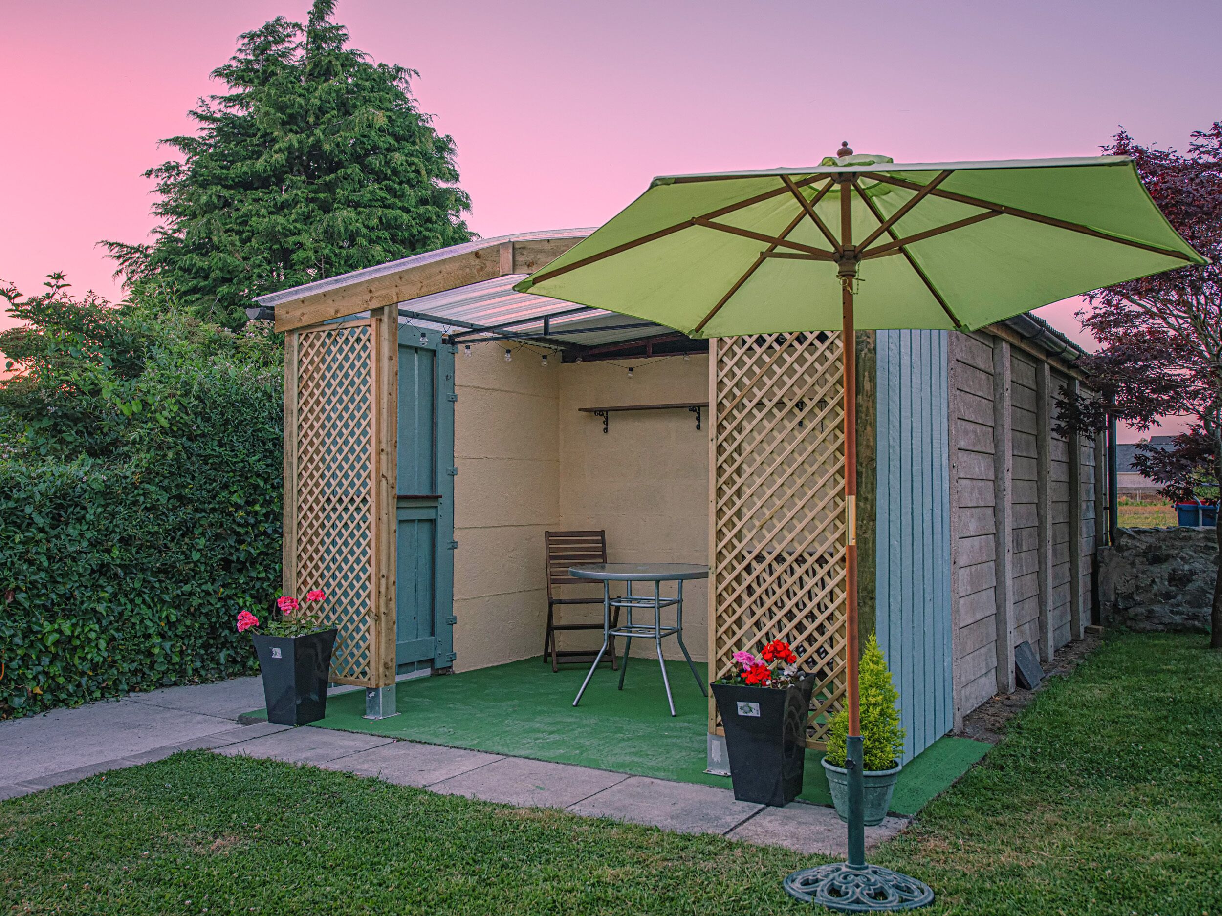 A small, enclosed patio area with a table and chairs, surrounded by a wooden fence and potted plants.