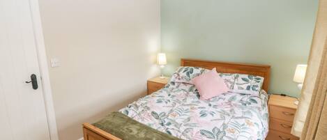 Une chambre à coucher avec un lit en bois, une literie à motifs floraux, deux tables de chevet avec des lampes, une porte et un mur de couleur vert clair.
