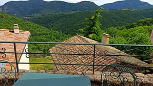 A balcony with a view of lush green hills and a tiled roof. - Gîte douillet pour 2 personnes (Pourchères)