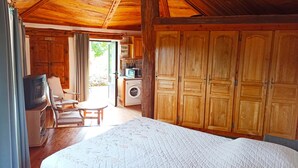A cozy room with a wooden ceiling, a bed, a television, a washing machine, and a dining area. - Gîte douillet pour 2 personnes (Pourchères)