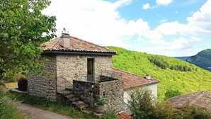 A stone cottage with a tiled roof, a small balcony, and a view of a lush green hillside. - Gîte douillet pour 2 personnes (Pourchères)