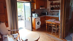 A compact kitchen with wooden cabinets, a washing machine, a microwave, and a dining area with a table and chairs. - Gîte douillet pour 2 personnes (Pourchères)